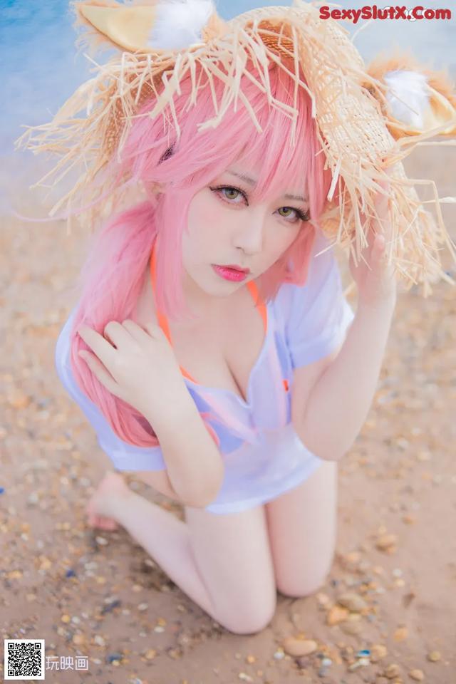 A woman with pink hair wearing a straw hat on the beach.