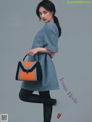 A woman in a black sweater and pink skirt holding a pink purse.