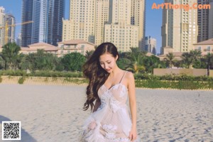 A woman in a white dress holding a surfboard on the beach.